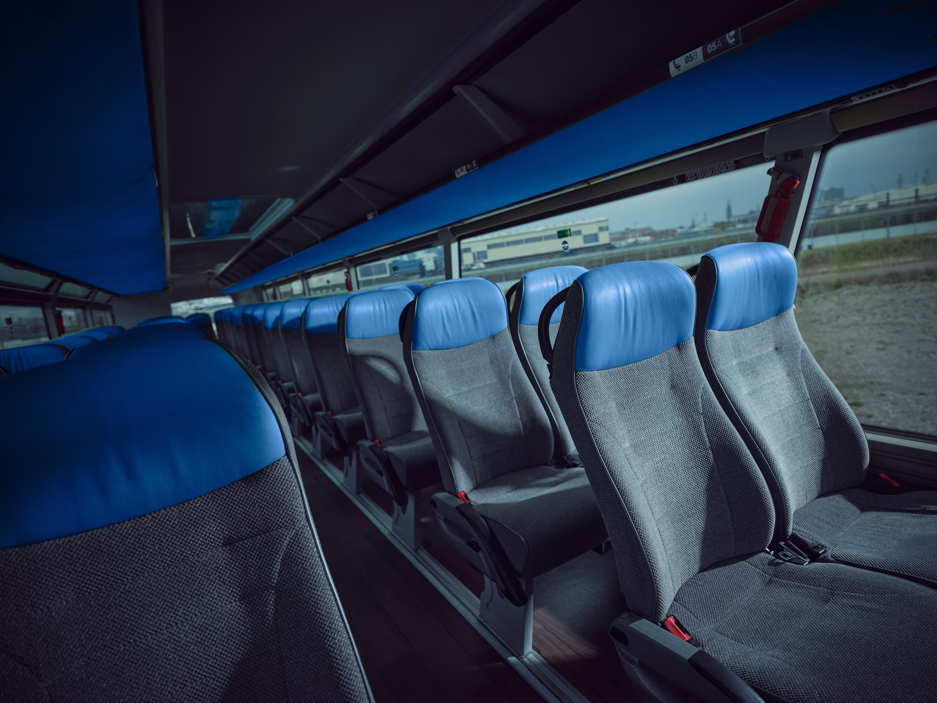 Blick durch den Mittelgang des Oberdecks eines Neoplan Skyliner Reisebusses mit grauen Sitzen und auffälligen blauen Kopfpolstern sowie einer blauen Verkleidung der Gepäckablagen unter der Decke.