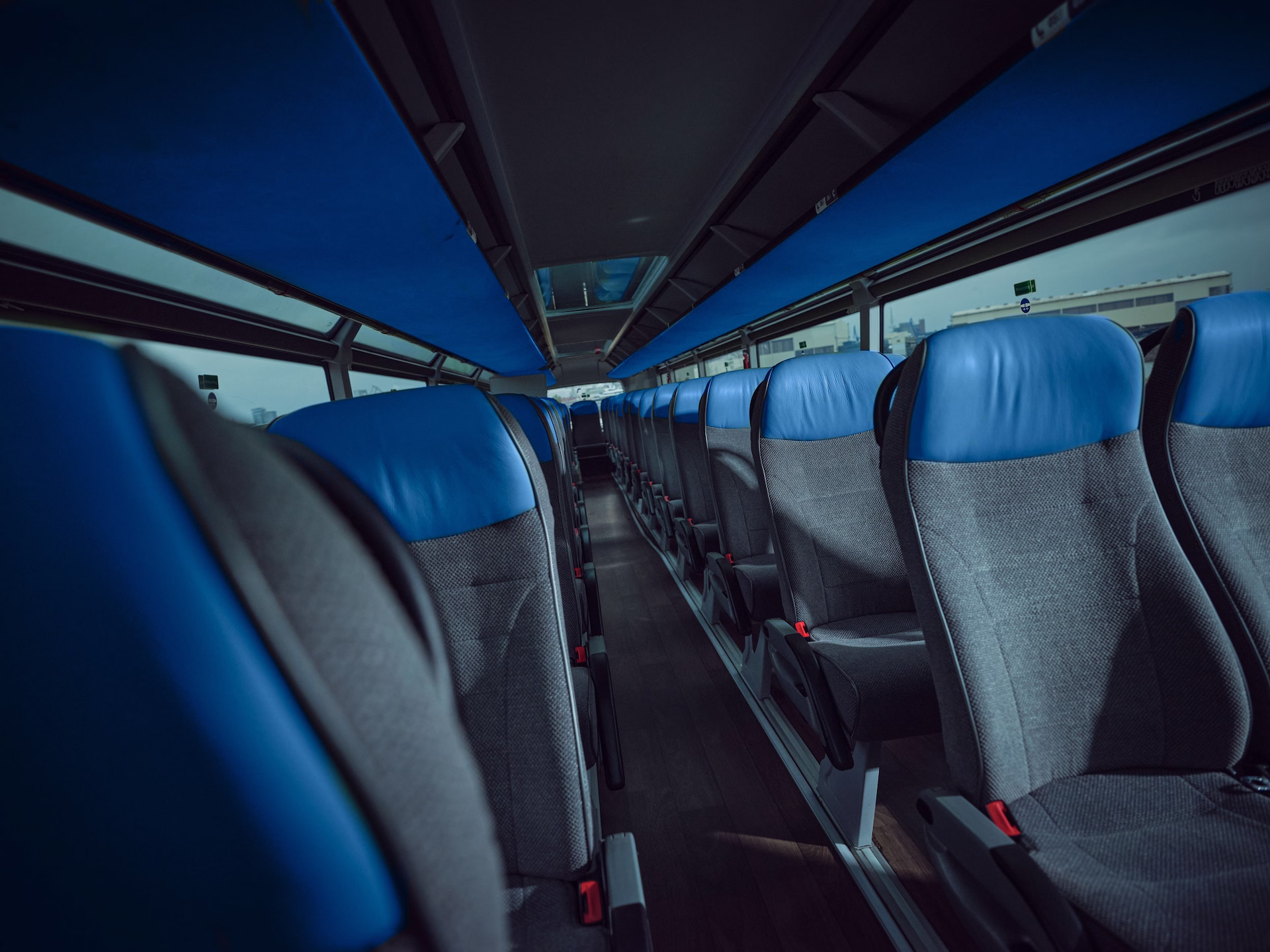 Blick durch den Mittelgang des Oberdecks eines Neoplan Skyliner Reisebusses mit grauen Sitzen und auffälligen blauen Kopfpolstern sowie einer blauen Verkleidung der Gepäckablagen unter der Decke.