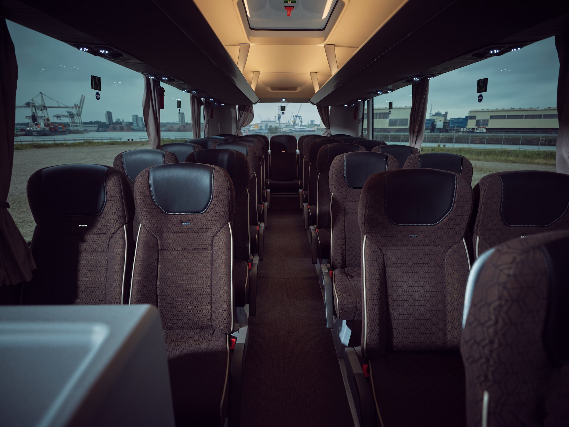 Blick von vorne durch den Reisebus-Mittelgang nach hinten auf die Sitzreihen und die Rückbank vor einer Hafenkulisse.