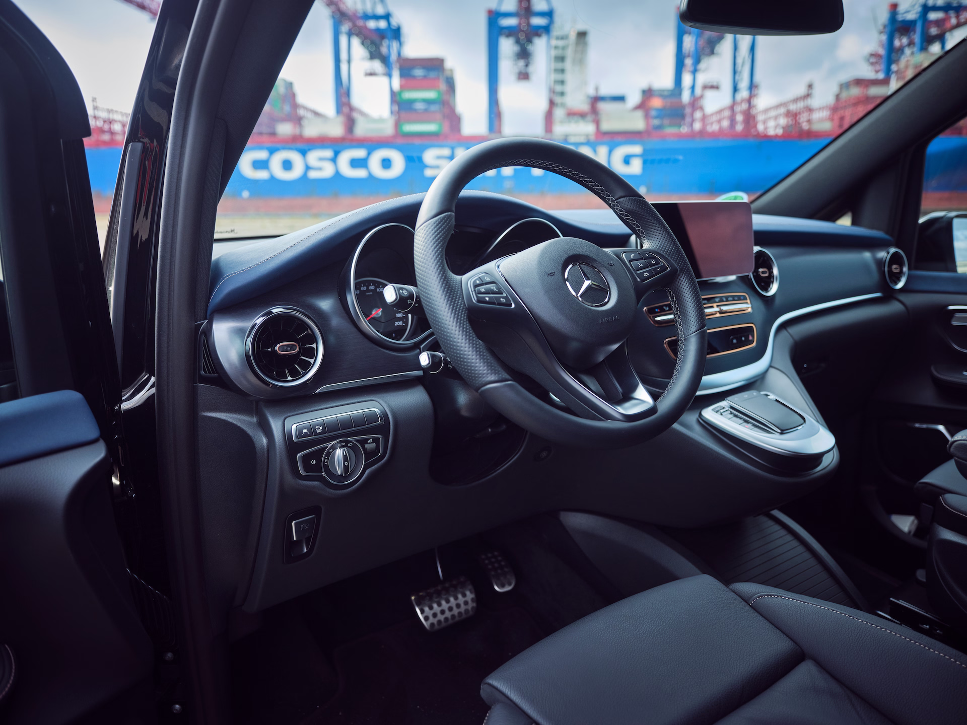 Fahrerbereich eines modernen Shuttle-Vans mit hochwertigem Cockpit und Blick auf ein Containerterminal im Hintergrund.