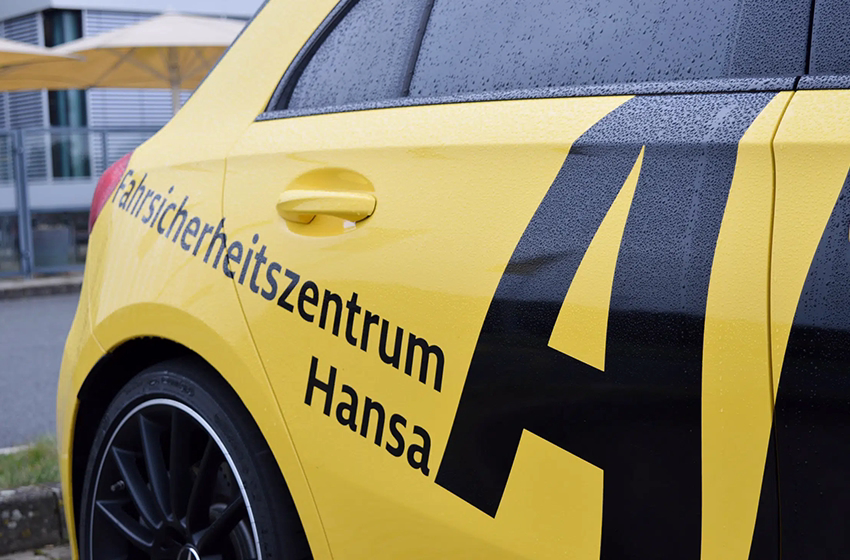 Gelbes Fahrzeug mit der Aufschrift „Fahrsicherheitszentrum Hansa“ an der Seite, bei Regen im Freien geparkt, im Kontext eines ADAC-Fahrtrainings der agt..