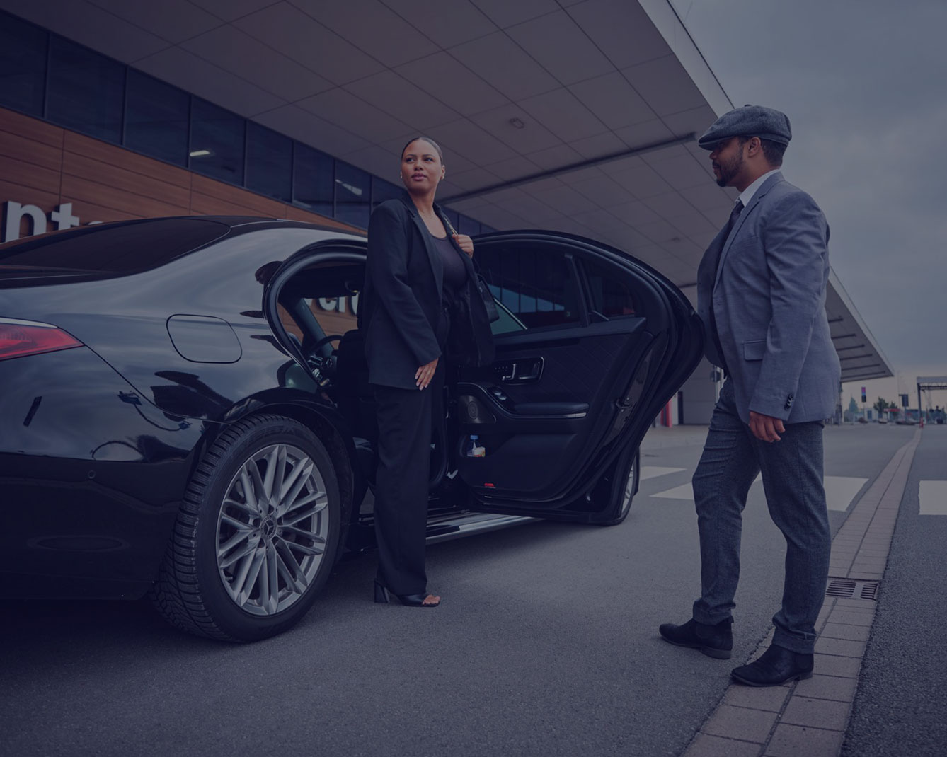 Geschäftskundin steigt vor einem Terminalgebäude aus einer Limousine aus und wird von einem Fahrer empfangen.