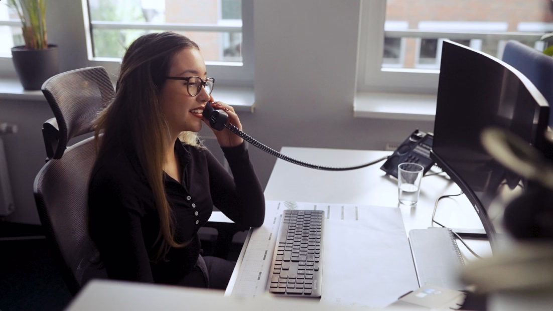 Mitarbeiterin telefoniert an ihrem Arbeitsplatz und bearbeitet Anfragen am Computer.