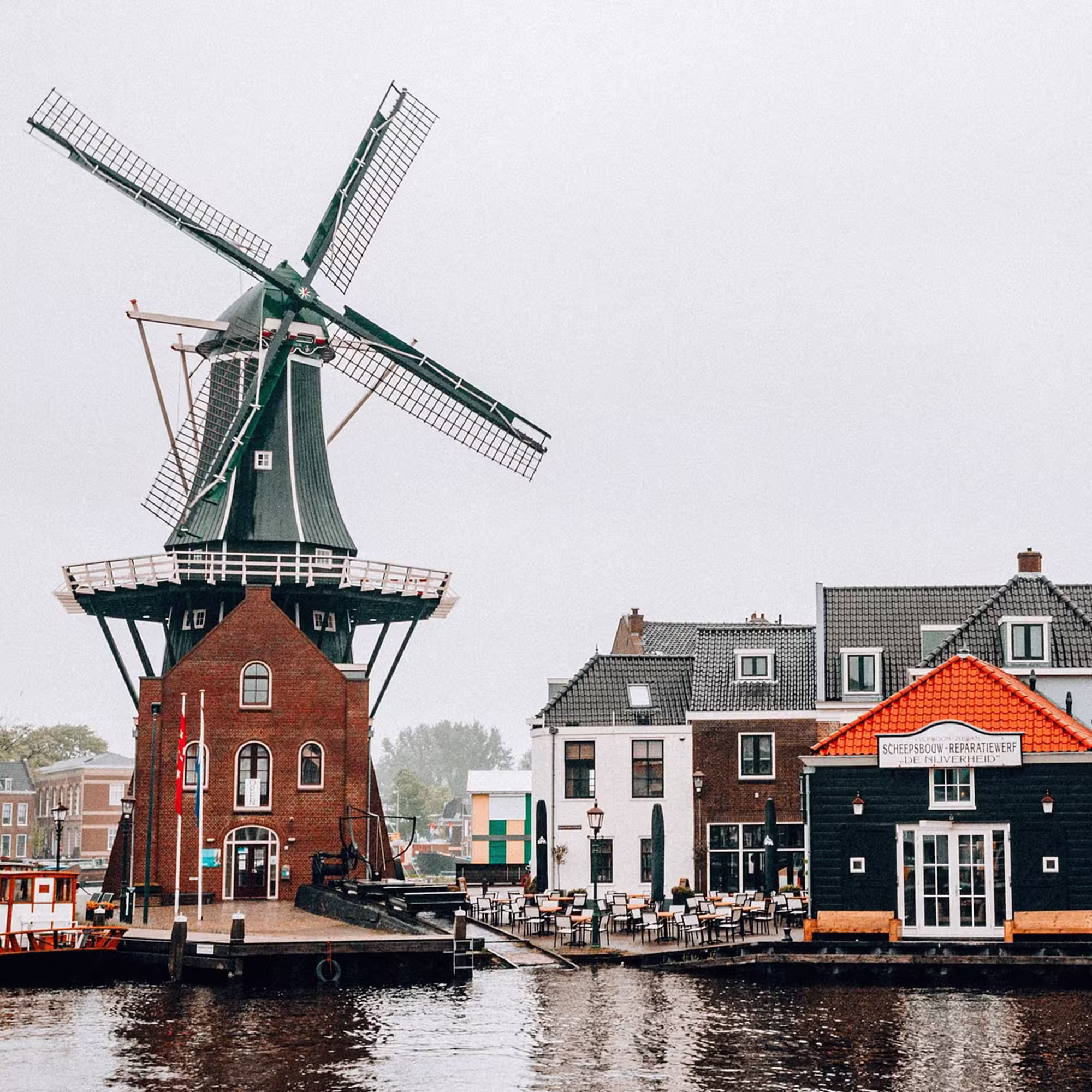 Historische Windmühle am Wasser in den Niederlanden, umgeben von traditionellen Häusern und einem kleinen Hafen.