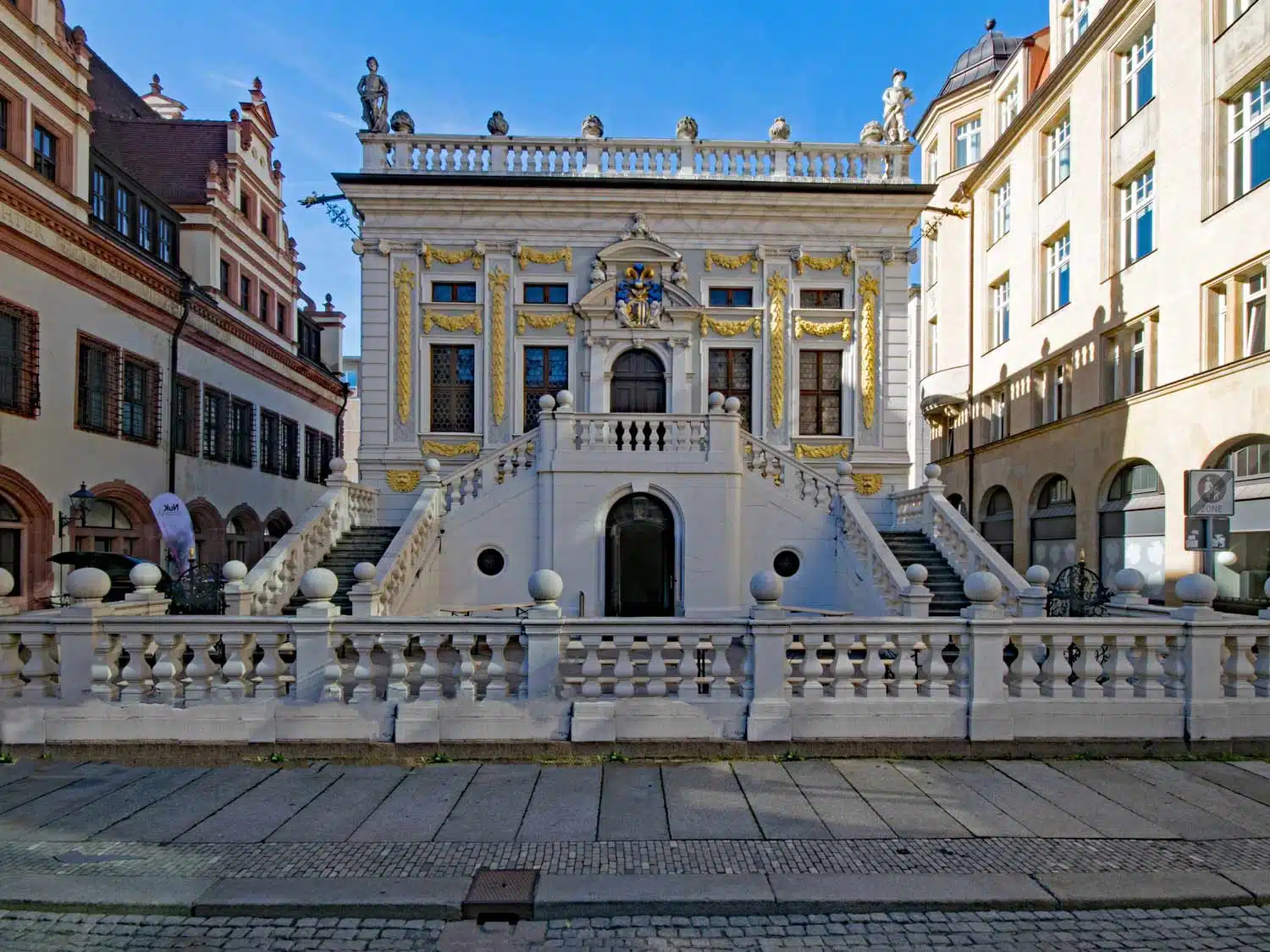 Historisches Barockgebäude mit prächtiger Fassade, vergoldeten Verzierungen und einer repräsentativen Freitreppe in der Leipziger Altstadt unter klarem blauem Himmel.