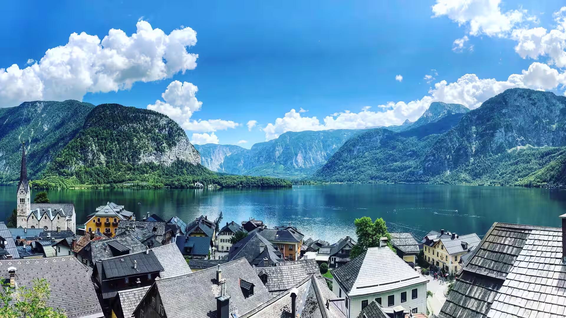 Blick über die Dächer von Hallstatt mit Kirchturm auf den Hallstätter See und die umliegenden Berge.
