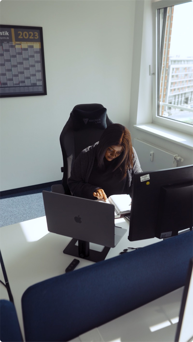 Mitarbeiterin arbeitet konzentriert an ihrem Schreibtisch und prüft Unterlagen am Computerarbeitsplatz.