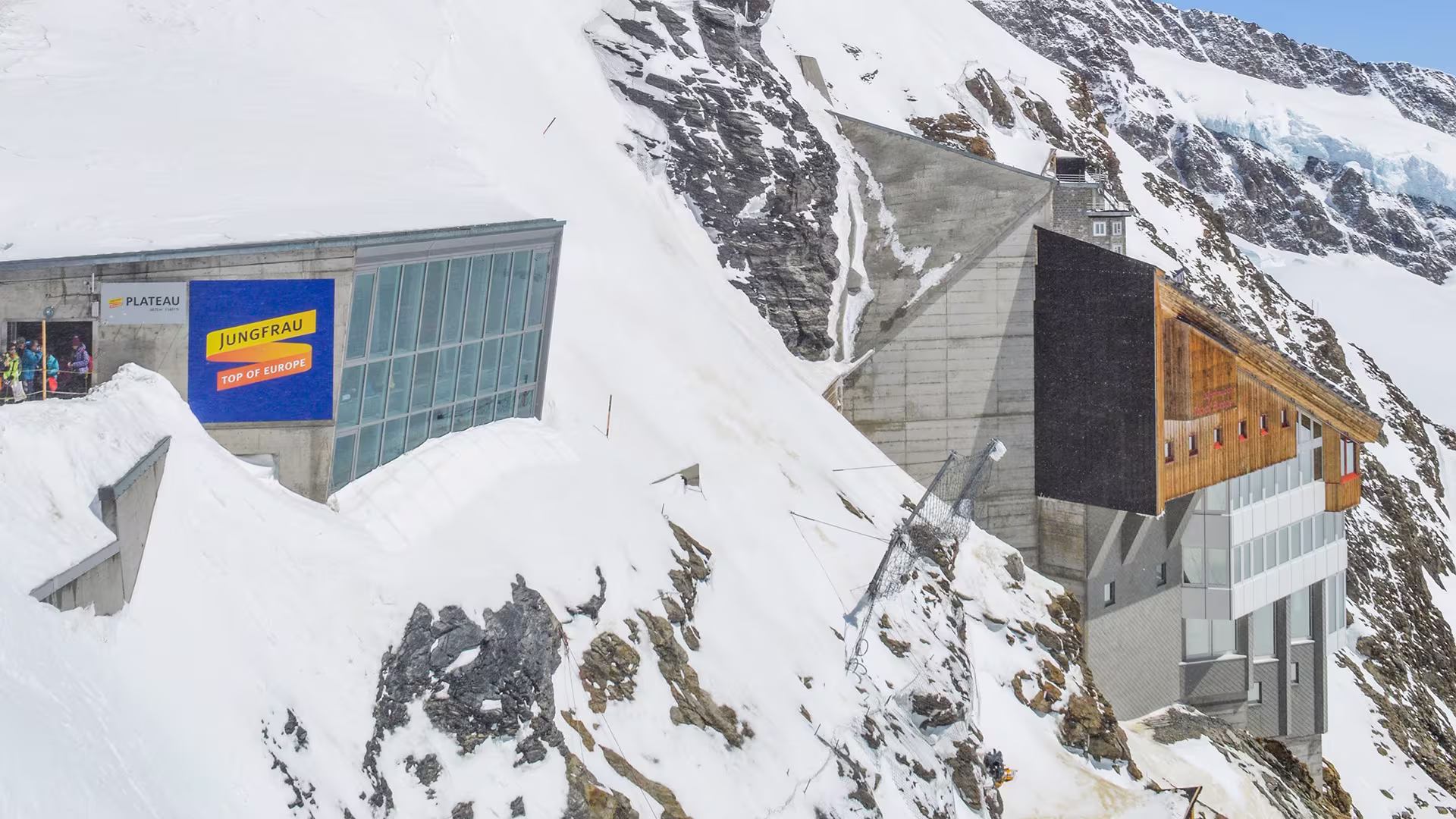 Gebäude auf dem Jungfraujoch mit Zugang zum Plateau und dem Berghaus „Top of Europe“ in verschneiter Hochgebirgslandschaft.