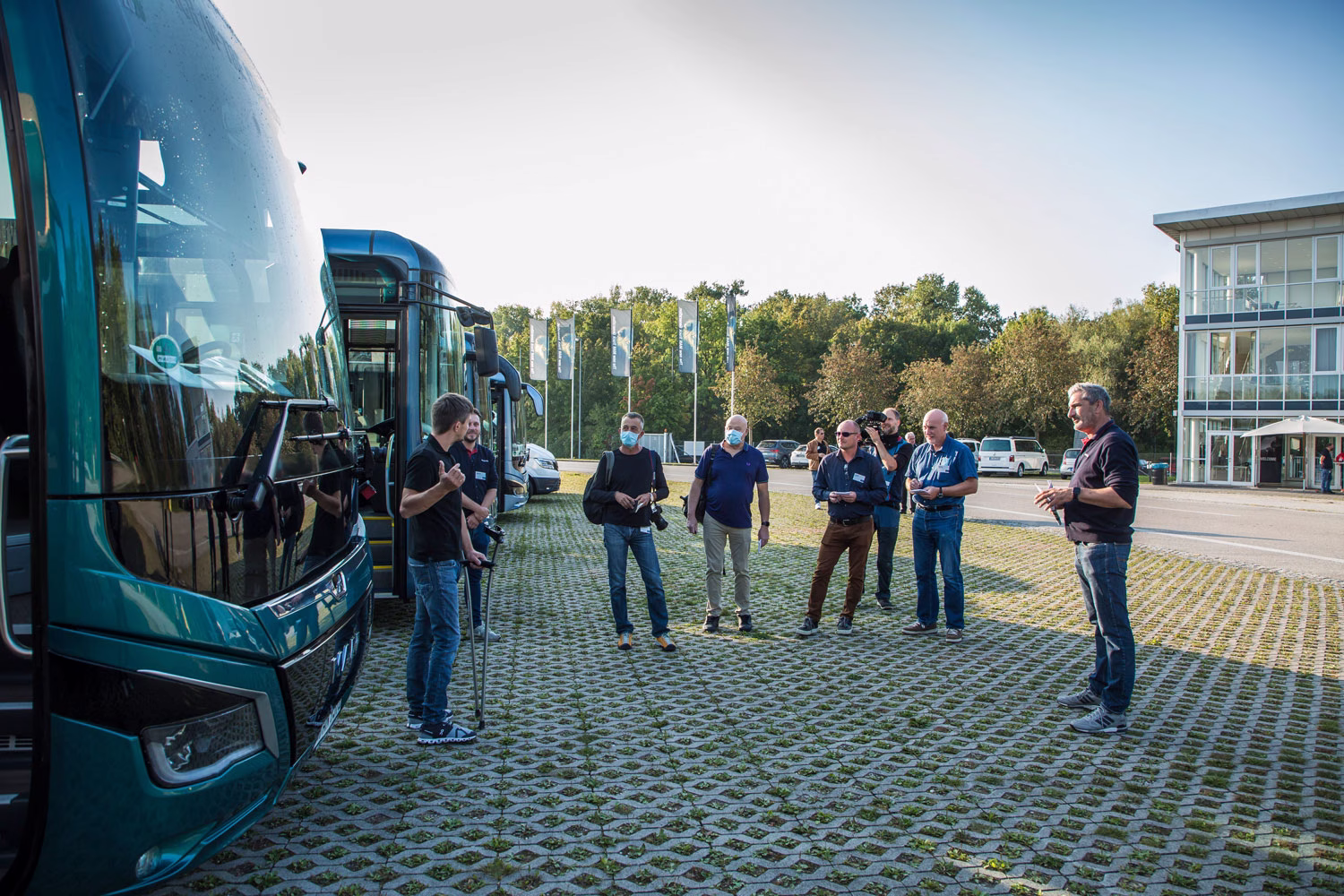 Teilnehmende einer Busveranstaltung stehen vor modernen Reisebussen und erhalten eine Einweisung oder Fahrzeugpräsentation im Freien.