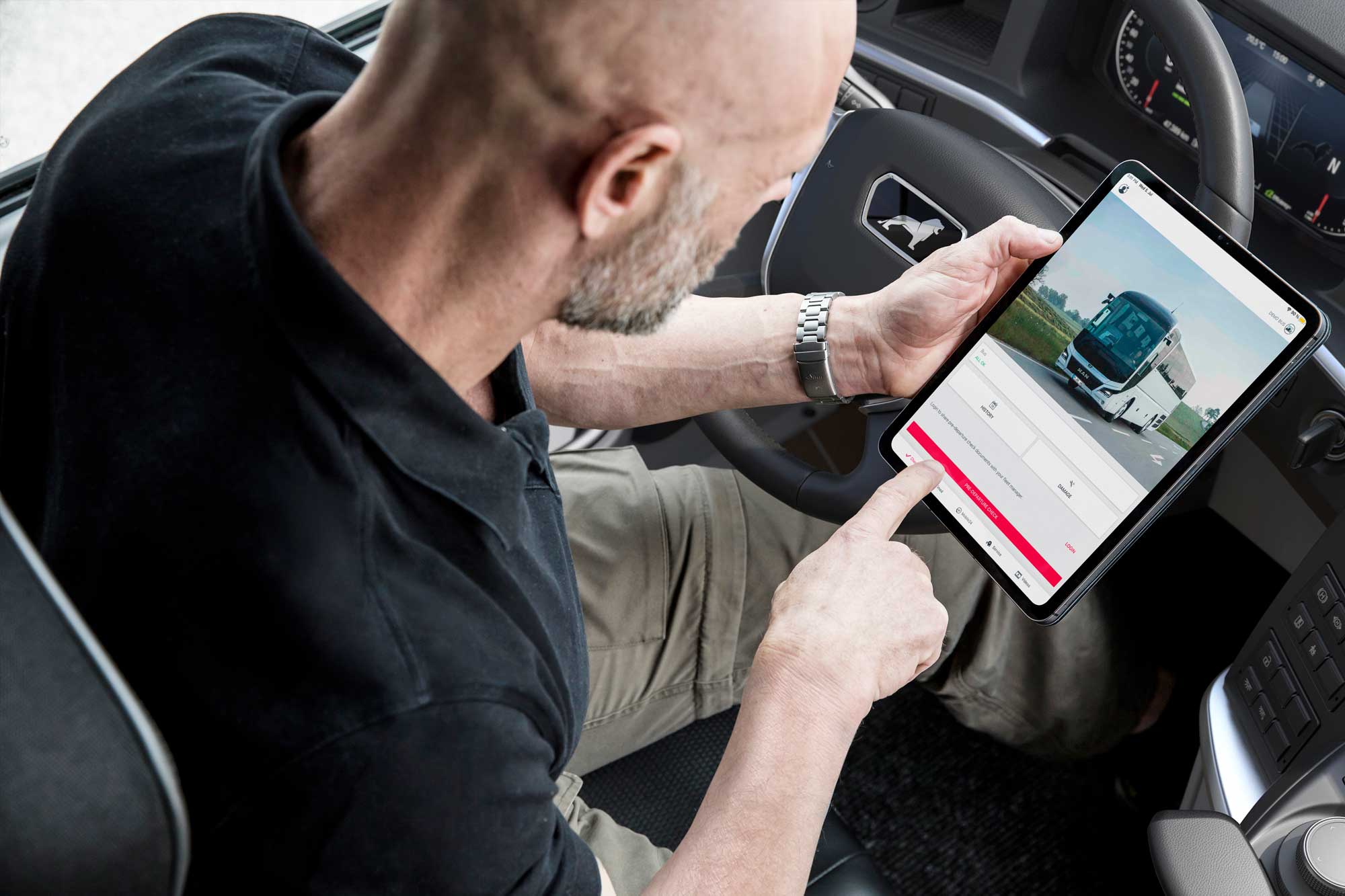 Ein Busfahrer sitzt im Fahrerbereich eines Reisebusses und bedient ein Tablet mit einer digitalen Anwendung zur Fahrzeug- oder Einsatzverwaltung. Die Szene verdeutlicht den Einsatz moderner Technologien im Busbetrieb, etwa für Fahrzeugchecks, digitale Dokumentation, Flottenmanagement oder die operative Steuerung von Fahrten.