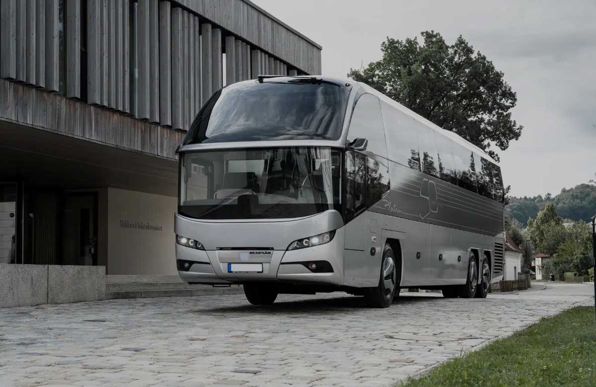 Moderner Reisebus steht vor einem Gebäude auf einer gepflasterten Straße.
