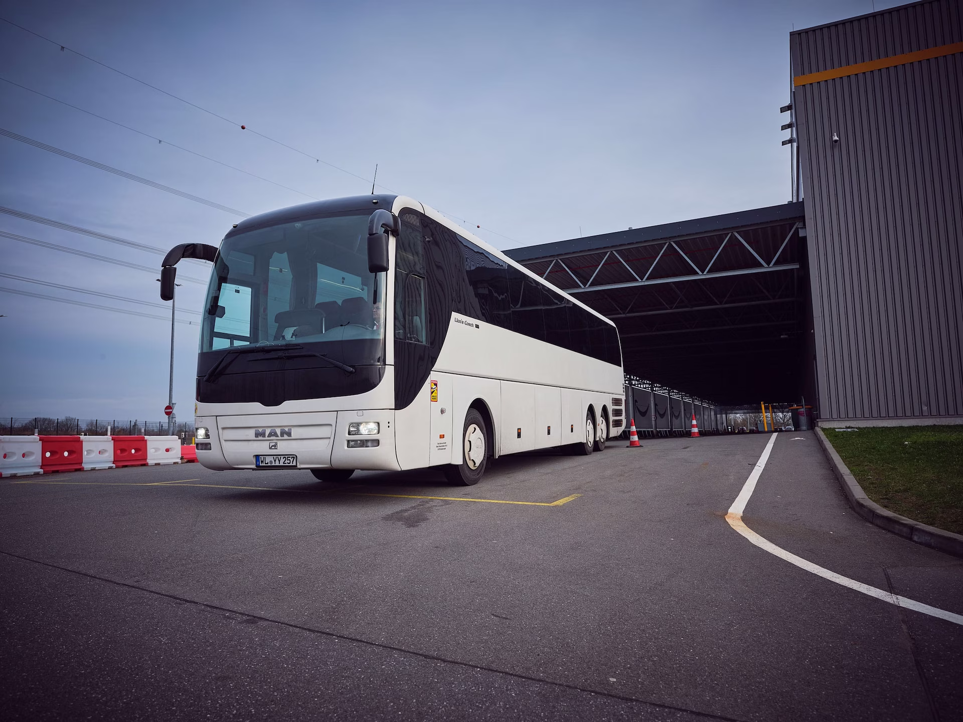 Weißer Reisebus steht vor einer modernen Halle und wartet auf den nächsten Fahrgast- oder Gruppentransfer.