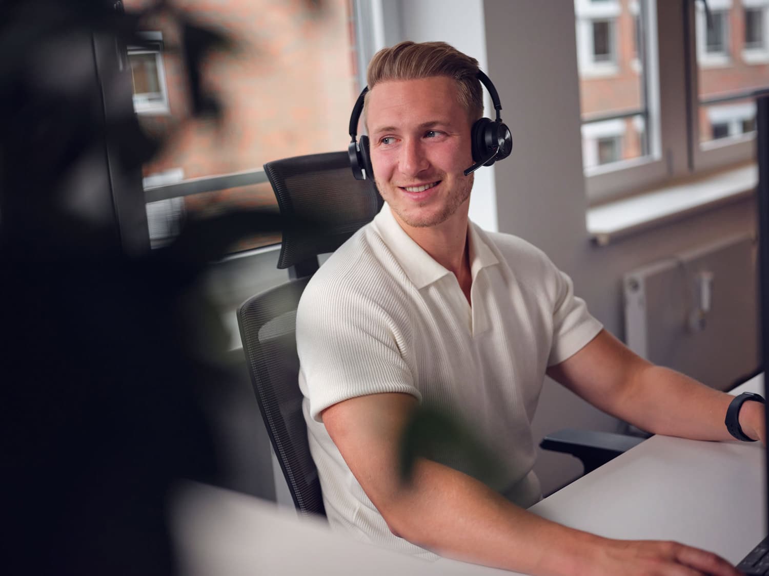 Mitarbeiter mit Headset sitzt am Arbeitsplatz und betreut Kundenanfragen telefonisch oder digital im Büro.