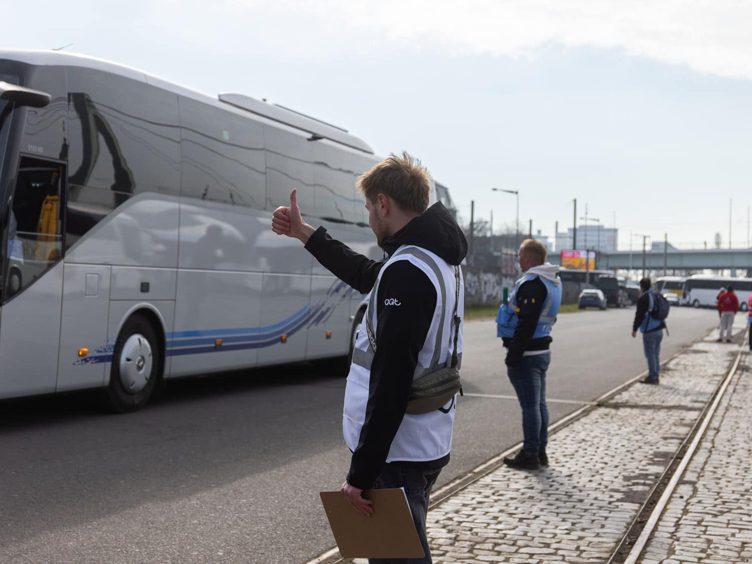 Mitarbeiter in Warnweste weist ankommende Reisebusse an einer Haltestelle ein.
