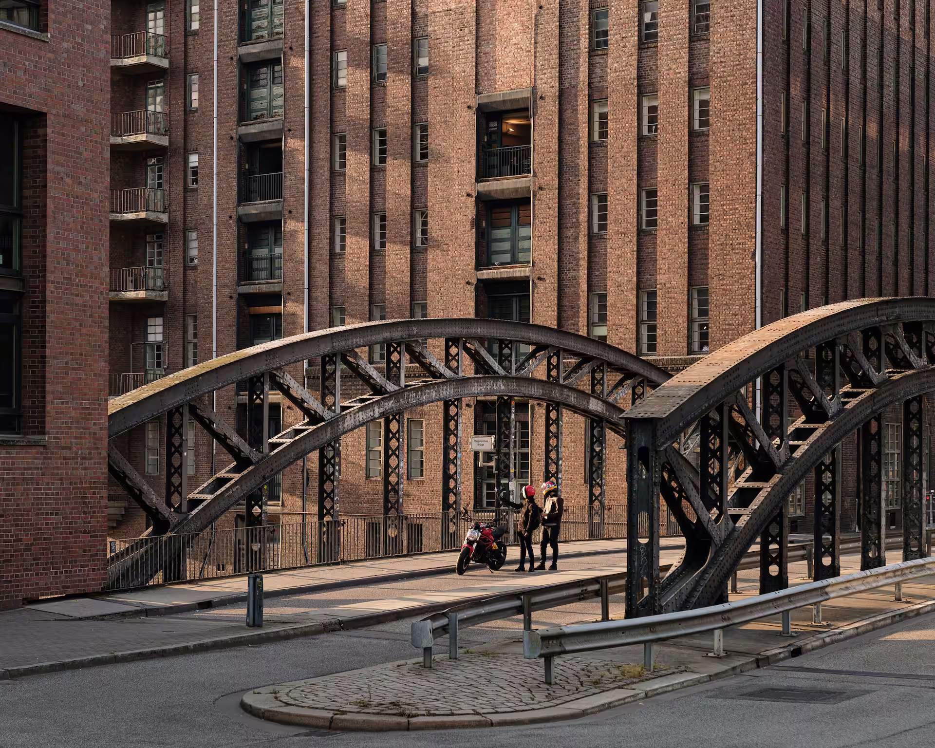 Stahlbrücke in der Hamburger Speicherstadt vor historischen Backsteingebäuden, mit zwei Personen und einem Motorrad auf der Brücke.