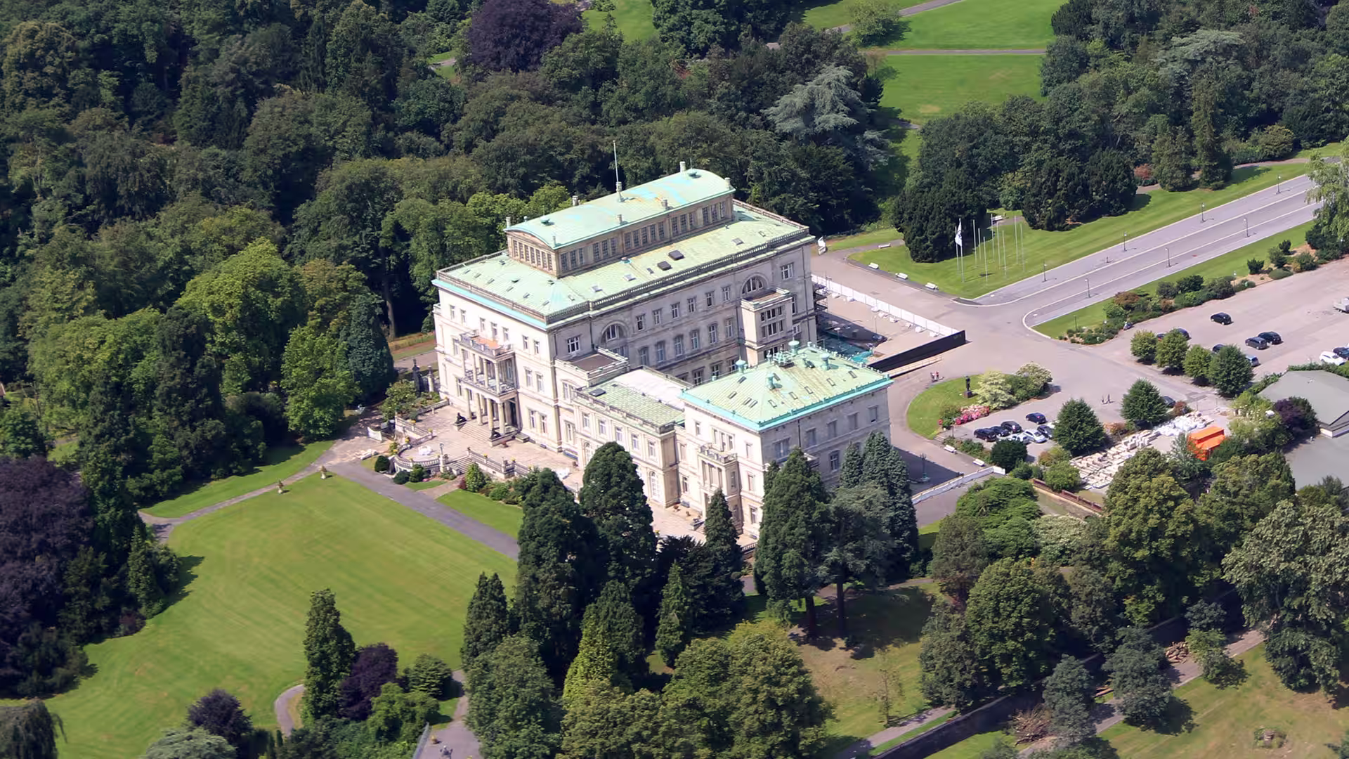 Luftaufnahme der Villa Hügel in Essen mit grünen Kupferdächern, umgeben von Park und Wald.