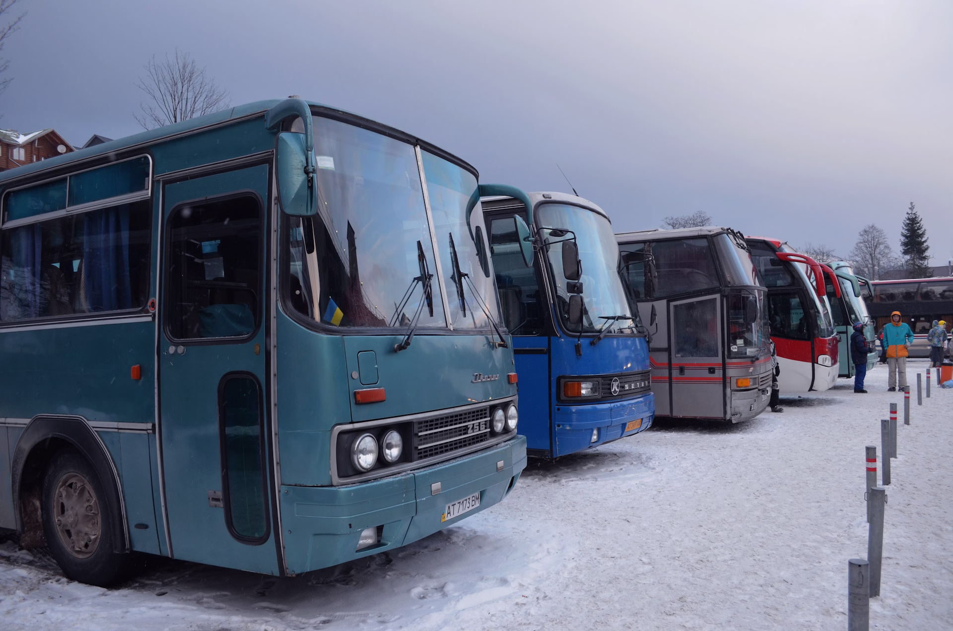 Mehrere Reisebusse stehen auf einem verschneiten Parkplatz in einer Reihe nebeneinander
